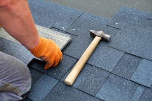 Contractor hands installing bitumen roof shingles using hammer in nails