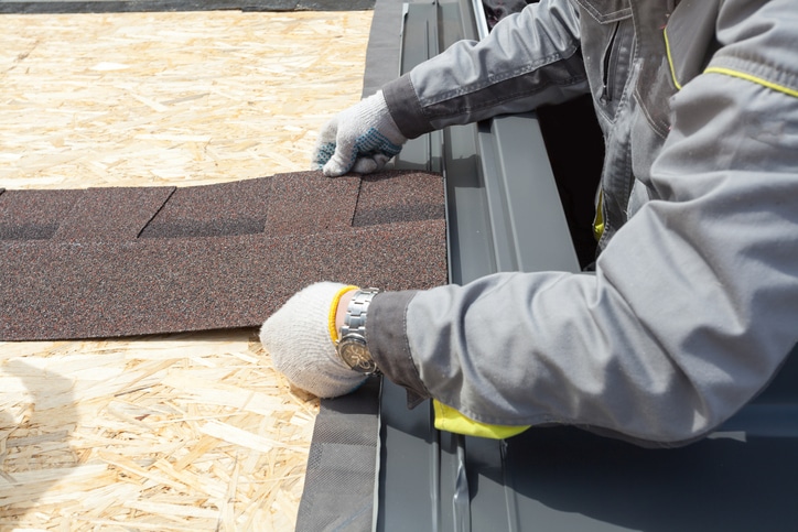 worker lays asphalt sheet on rooftop